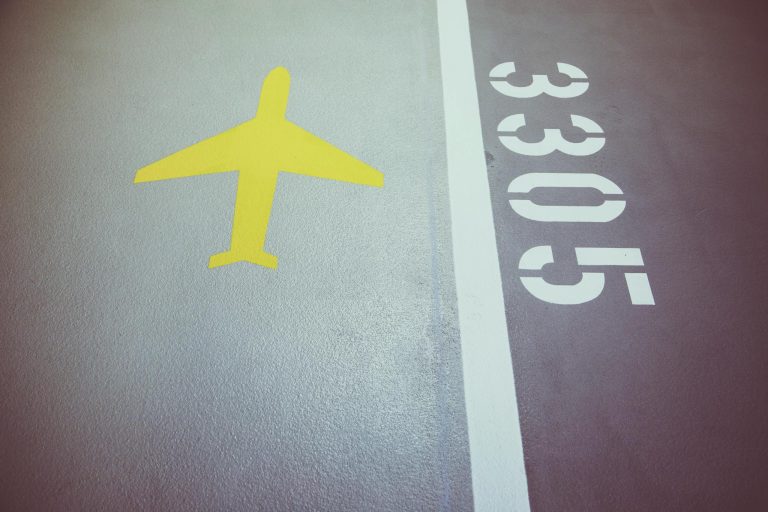 A close-up of a yellow airplane symbol and white numbers on textured gray asphalt, presenting Belgrade Airport Transfer Services