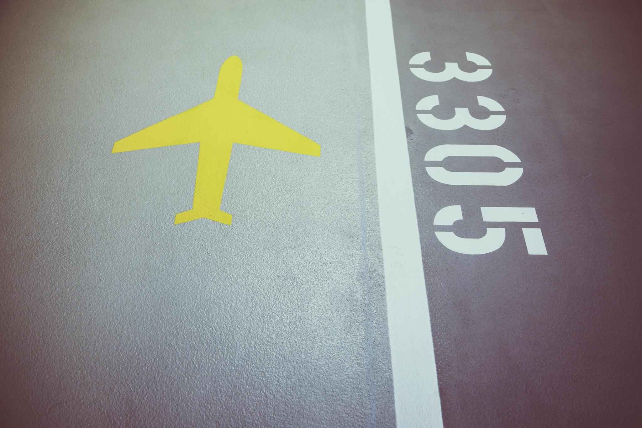 A close-up of a yellow airplane symbol and white numbers on textured gray asphalt, presenting Belgrade Airport Transfer Services