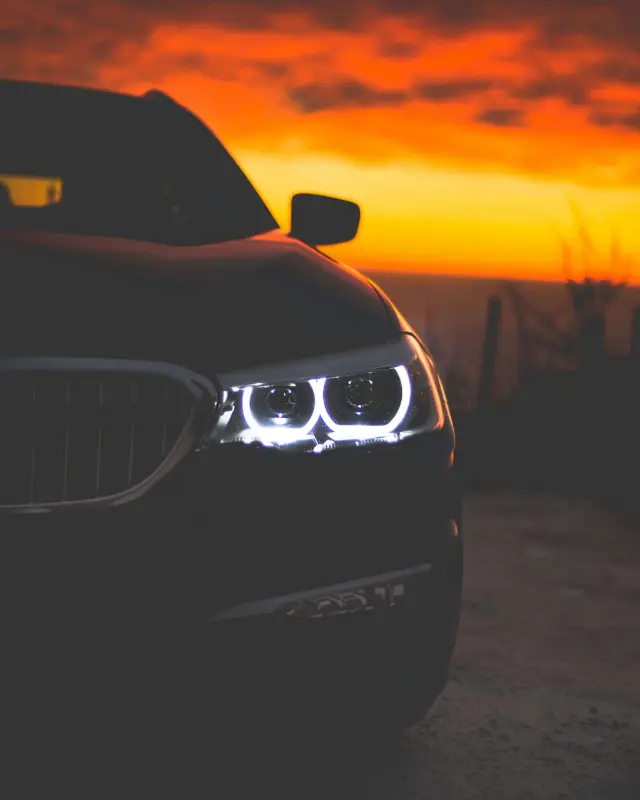 Silhouette of a luxury car headlight against a golden sunset sky.