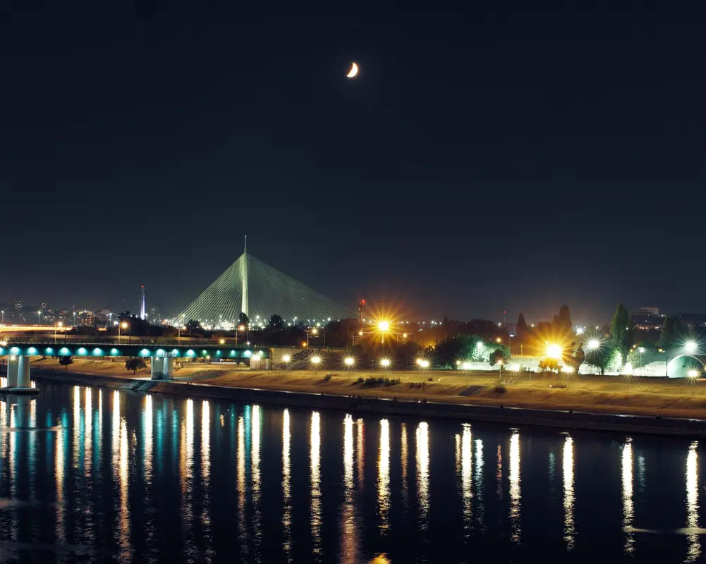 Illuminated Ada Bridge in Belgrade reflecting in the Sava River at night.